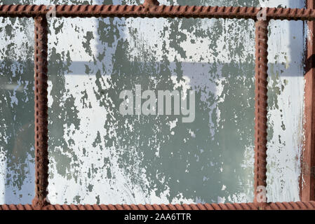 Old window painted by white paint behind a rusty brown bars on a sunny day. Abstract background Stock Photo