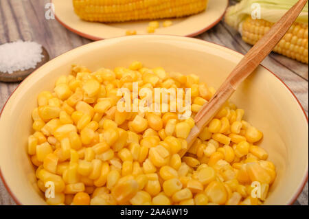 Grains of sweet corn in a plate with a wooden spoon and ears of corn on the table. Healthy diet. Fitness diet. For a sweet treat. Close up Stock Photo