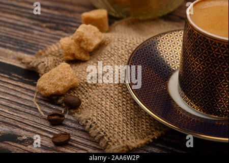 A Cup of coffee, pieces of brown sugar in a sugar bowl, coffee beans on a wooden background. Close up Stock Photo