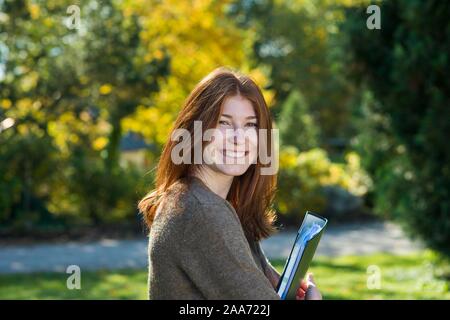 Young smiling red-haired woman, student, pupil holds folder, Bavaria, Germany Stock Photo