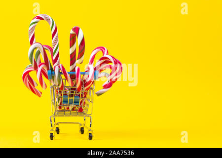 Mini shopping cart with Christmas candy canes on yellow background Stock Photo
