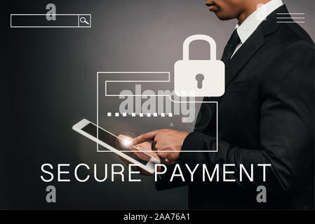 partial view of african american businessman using digital tablet on dark background with secure payment illustration Stock Photo