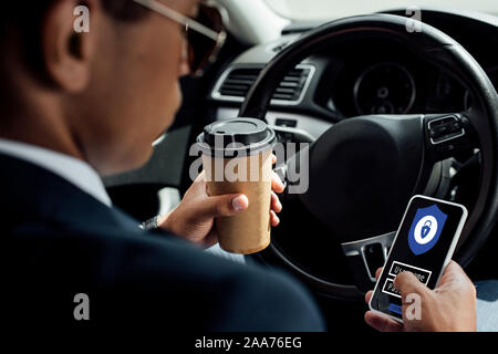 back view of african american businessman using smartphone with secure access illustration and drinking coffee in car Stock Photo