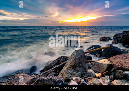 Ocean water splash on rock beach with beautiful sunset sky and clouds. Sea wave splashing on stone at sea shore on summer. Nature landscape. Tropical