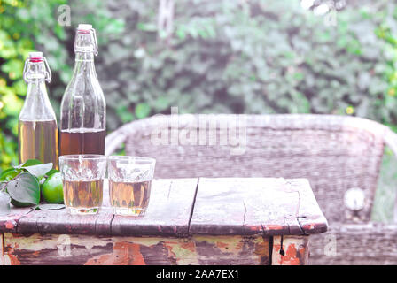 apple cider, bottled, and glasses, stands on an old wooden table. Decorated with apples. Summer rest. Semester evening. Against the background of gree Stock Photo
