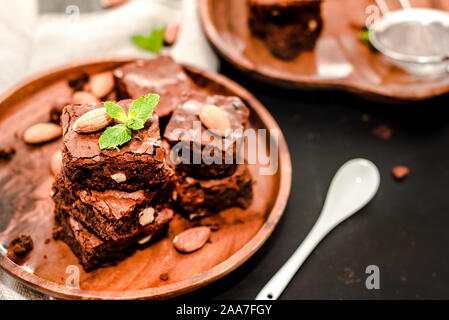 Piece of stack homemade dark chocolate brownies topping with almond slices and mint on wood table with copy space. Stock Photo