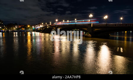 Buses leave light trails in a long exposure night photo of Battersea Bridge, Chelsea riverside and the River Thames in west London. Stock Photo