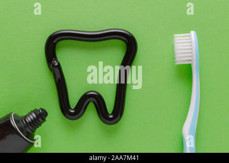 a tooth from black toothpaste, teeth care concept, toothbrush on green background Stock Photo