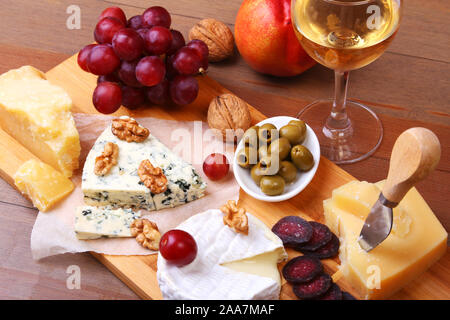 Assortment of cheese with fruits, grapes, nuts and cheese knife on a wooden serving tray Stock Photo