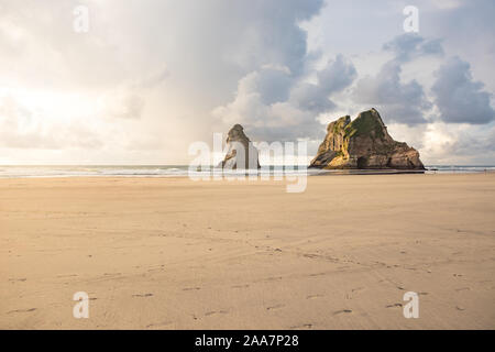 View on famous rocks of Wharariki Beach in Golden Bay in New Zealand during sunset with dramatic clouds. Footprints in sand in foreground. Stock Photo