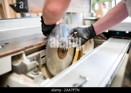 Carpenter in a workshop changing a circular saw blade in a close up on the machine and his gloved hands Stock Photo