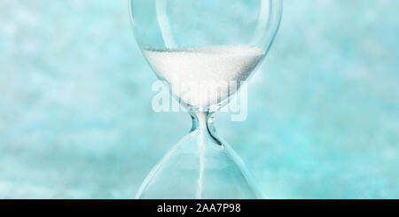 Hourglass panorama. Time is running out concept. A close-up of a sand clock on a teal blue background with copy space Stock Photo