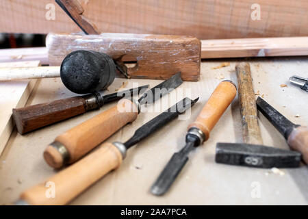 Assorted carpenters tools lying scattered on a workbench in a workshop in a close up view on different chisels and hammer Stock Photo