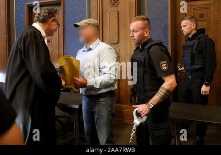 20 November 2019, Mecklenburg-Western Pomerania, Schwerin: Matthias Macht (l-r), defense attorney, welcomes the defendant, a former member of a police special task force (SEK), while he is brought into the courtroom by other police officers. In the trial in connection with the right-wing Prepper group 'Nordkreuz', the 49-year-old accused is accused of illegally stockpiling weapons and thus of violating the Weapons Act, the War Weapons Control Act and the Explosives Act. Preppers are people who prepare for the collapse of our civilization through political upheavals, wars or natural disasters ( Stock Photo