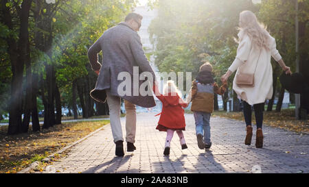 Happy family are walking together in the park. Mom, Dad, son and daughter are running along the sidewalk. Stock Photo