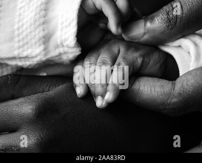 A black mom holding her baby's tiny hand and the sister holding the hand in monochrome Stock Photo