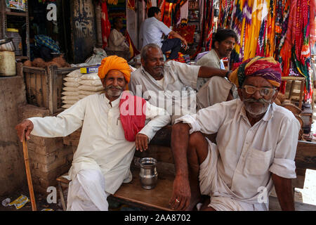 Bikaner, Rajasthan, India: four Indian men happy smile while sitting in front of a textile shop Stock Photo