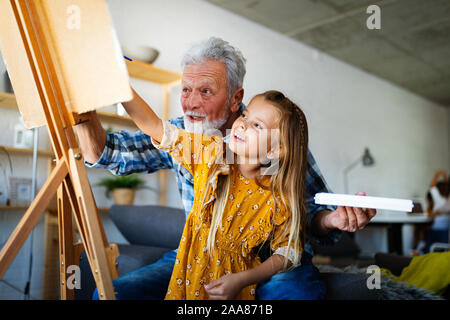 Senior man with child painting on canvas. Grandfather spending happy time with granddaughter. Stock Photo