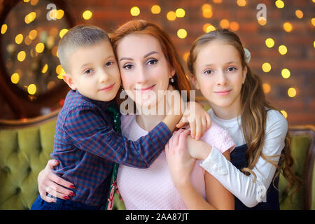 Portrait of a happy family. Mom with her beloved children sits on the sofa near the festive Christmas tree. Waiting for the holiday Stock Photo