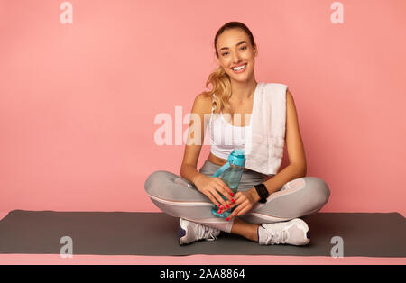 Positive Girl Sitting On Fitness Mat Resting Over Pink Background Stock Photo