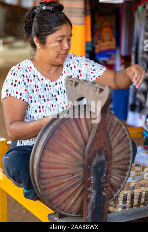 Older Burmese female weaver uses a spinning wheel to create thread for weaving traditional fabrics of the Bagan (Pagan) region of Myanmar (Burma) Stock Photo