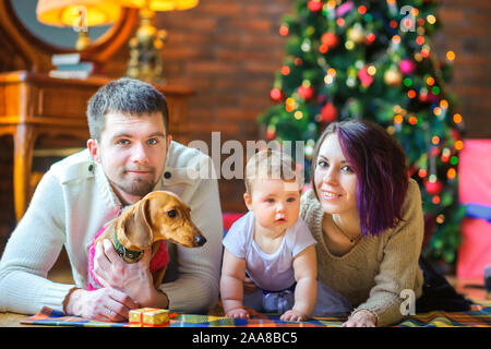Happy family with a puppy lie on the floor near the festive Christmas tree. Holidays Stock Photo