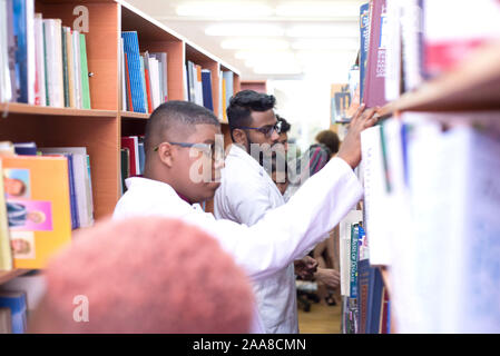 medical university students in a library looking for medical literature. Young people in white coats, mixed race. Stock Photo