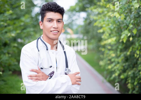 Portrait of a young handsome mexican doctor. A guy in a white coat with a stethoscope. Outdoor in Stock Photo