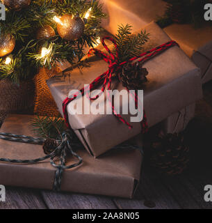 Night scene of Christmas presents wrapped in brown paper and tied with string  with decorated tree in background Stock Photo