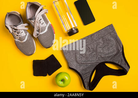 Fitness accessories on a yellow background. Sneakers, bottle of water, smart and sport top. Top view. Still life Stock Photo