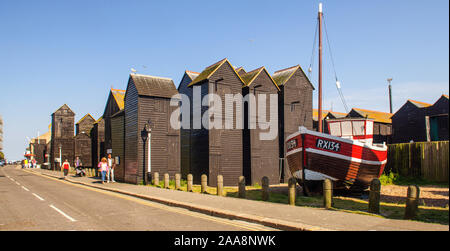 Hastings, England, UK - June 8, 2013: Tourists walk past the traditional fishermen's 'Net Shops' sheds and a beached fishing boat at Rock-a-Nore in Ha Stock Photo