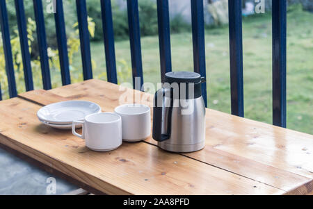 Close-up of white color empty plates, coffee cups and insulated hot drink container on cafe table of a coffee shop balcony isolated background. Place Stock Photo