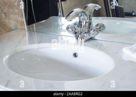 Bathroom interior with white sink and faucet, white washbasin, faucet, faucet, in the plumbing shop, close-up, with part of the mirror Stock Photo