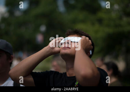 Young man looking up at solar eclipse wearing paper protective glasses Stock Photo