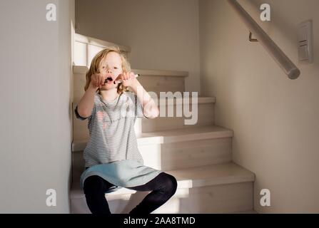 young girl making funny faces whilst drawing on her face at home Stock Photo