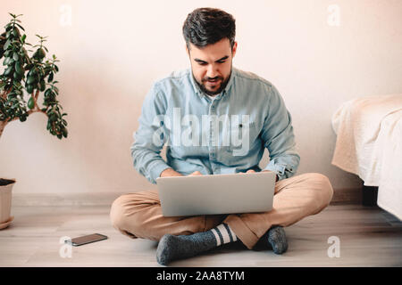 Young man using laptop computer while sitting on floor at home Stock Photo