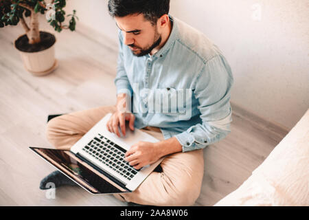 Serious man using laptop computer while sitting on floor at home Stock Photo