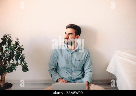 Happy businessman using laptop computer while sitting on floor at home Stock Photo