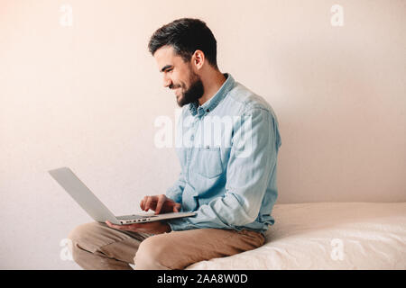 Happy man using laptop computer while sitting at home against wall Stock Photo