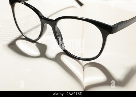 Heart made of shadow and glasses on opened book, close up Stock Photo