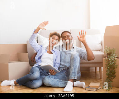 Spouses Using Tablet Sitting Among Moving Boxes Discussing Renovation Indoor Stock Photo