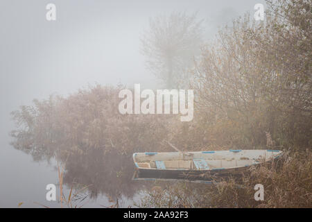 Old row boat at the waterfront in a misty frozen scenery early in the morning, picture taken at lake Kotermeerstal the Netherlands, province Overijsse Stock Photo
