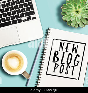 top view of words NEW BLOG POST written on spiral notepad on desk with laptop and potted plant Stock Photo