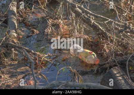 Empty floating plastic soft drink bottle in drainage ditch reflecting sky and background. Brand unidentified hence RM. Caught up metaphor, entangled. Stock Photo