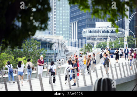 (Focus on the background) Defocused crowd of local people and tourists walking on a bridge in Singapore. Stock Photo