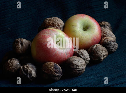 closeup of red apple among walnuts on green background Stock Photo
