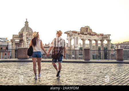 Young couple tourist walking towards Roman Forum at sunrise. Historical imperial Foro Romano in Rome, Italy from panoramic point of view. Stock Photo