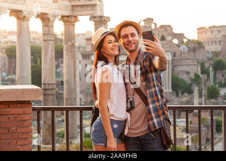 Young couple tourist looking at Roman Forum at sunrise and taking selfie. Historical imperial Foro Romano in Rome, Italy from panoramic point of view. Stock Photo