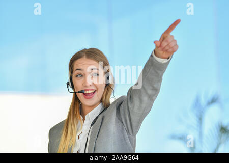 Photo of customer support or sales agent. Female caller or receptionist phone operator pointing with the finger. Copy space for some text, advertising Stock Photo