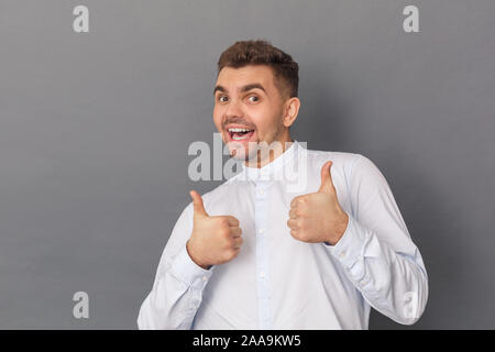 Freestyle. Young man studio standing isolated on grey showing thumbs up smiling playful Stock Photo